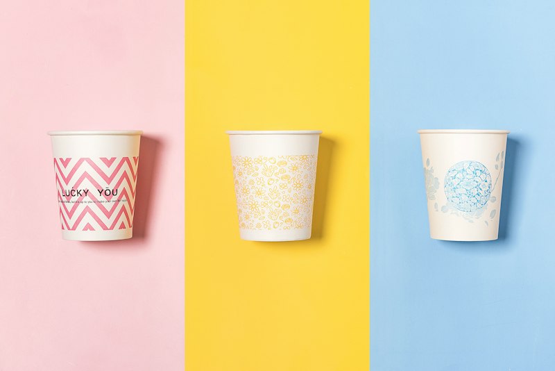 Three differently colored paper cups with custom printed designs, showcasing flexographic and offset printing results