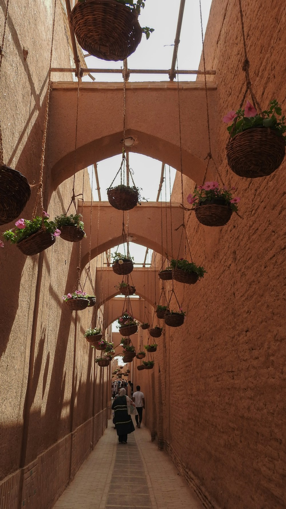 a narrow walkway with hanging baskets of flowers