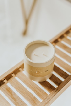 A chic, minimalistic scented candle in soft pastel tones on a warm wooden surface