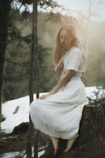 a woman in a white dress sitting on a tree stump