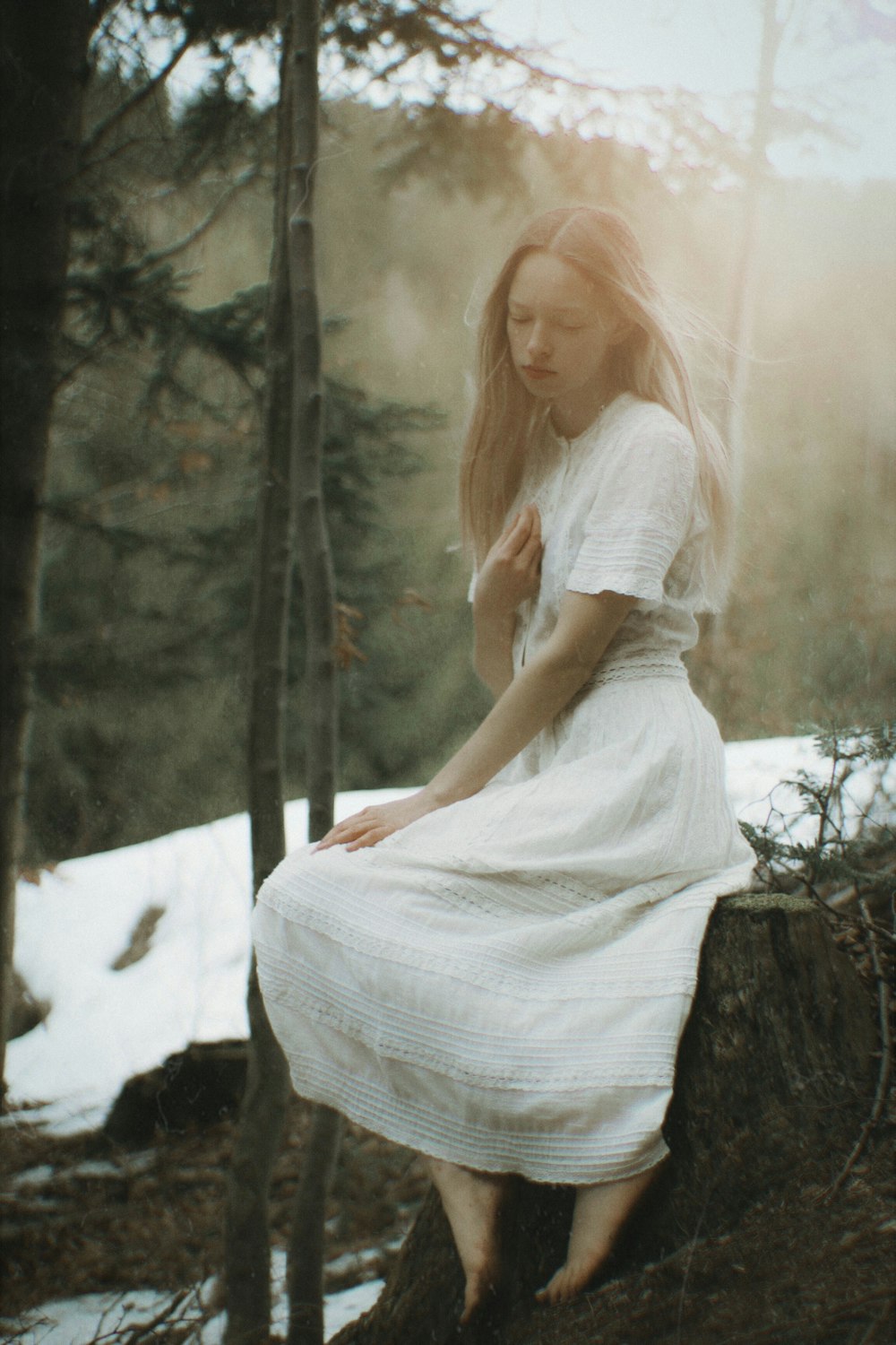 a woman in a white dress sitting on a tree stump