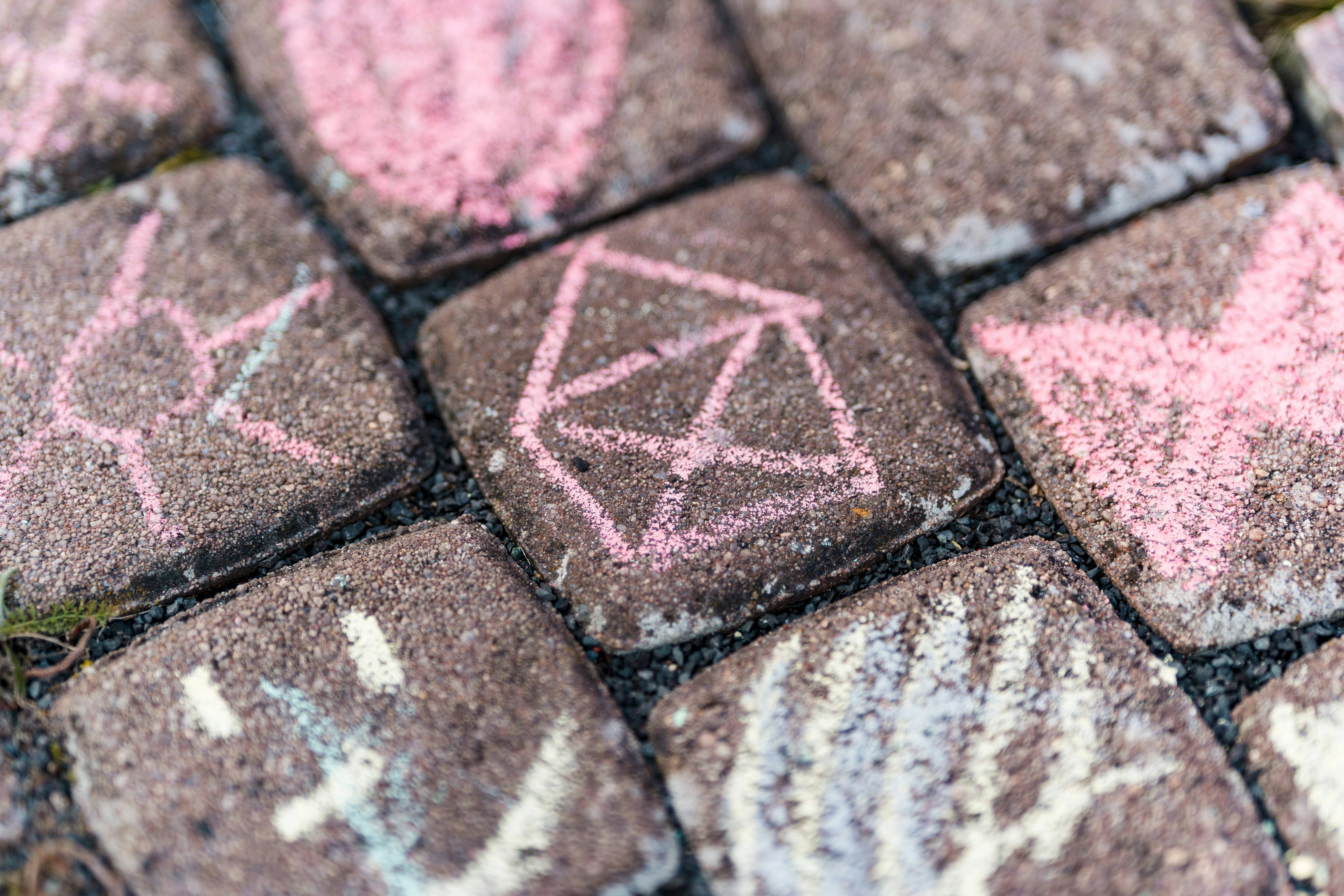 A sidewalk covered in colorful chalk drawings, one of them of a house