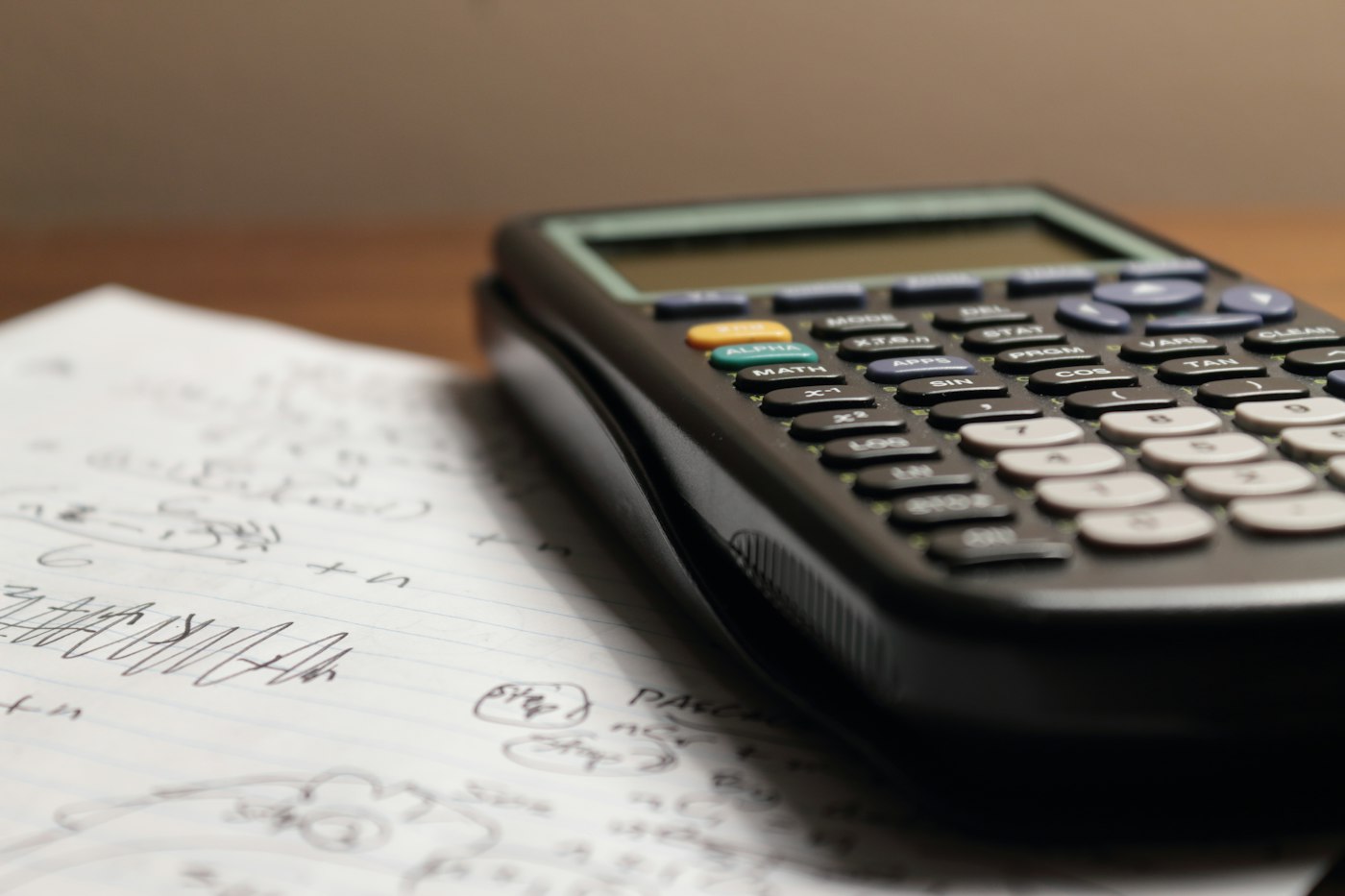 A black calculator rests on lined paper covered with handwritten calculations.