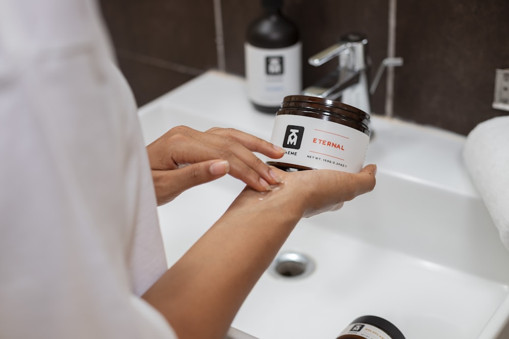 a person holding a jar of peanut butter in front of a sink