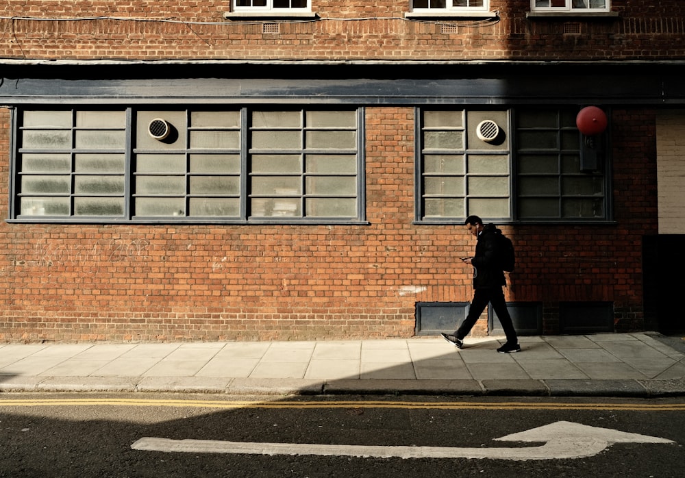 a man walking down a street past a tall brick building