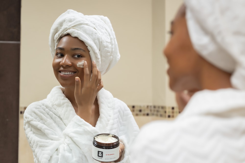 a woman with a towel on her head and a jar of cream on her face