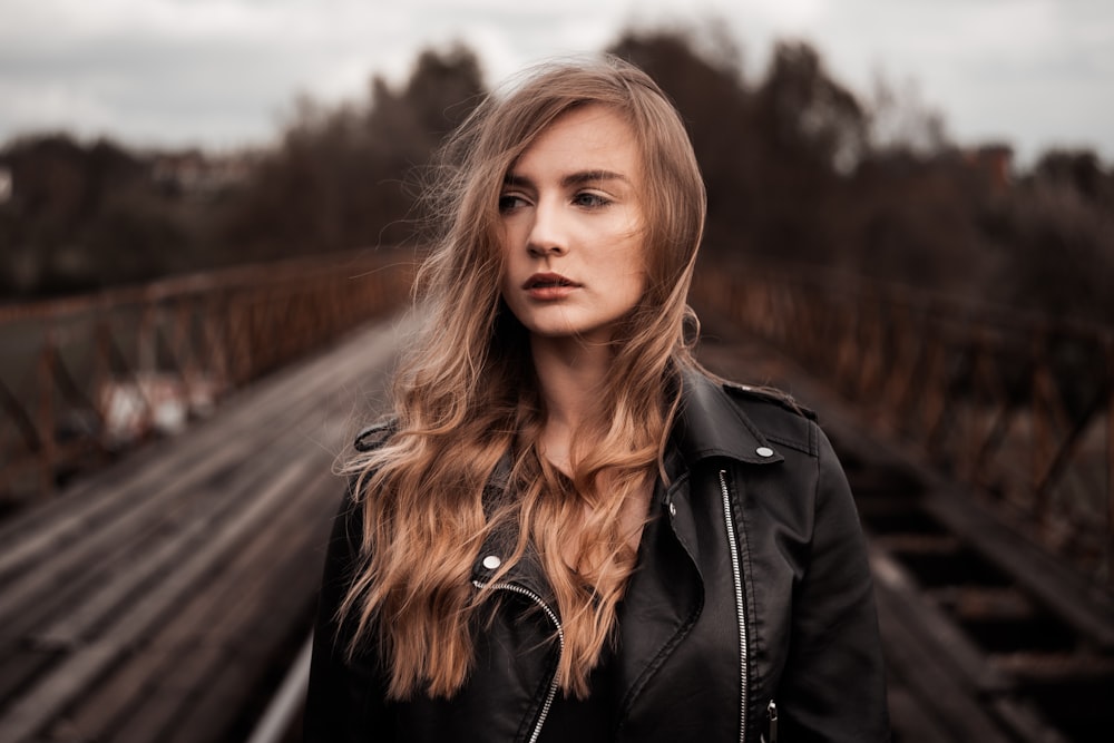 a woman in a black leather jacket standing on a bridge