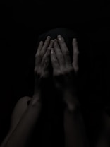 A pair of hands covering a face in a dark, shadowy environment, creating a sense of mystery or concealment.