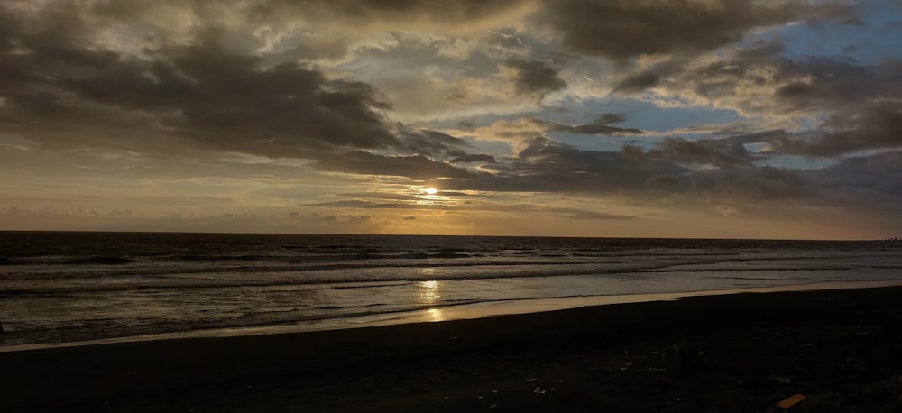 the sun is setting over the ocean on a cloudy day