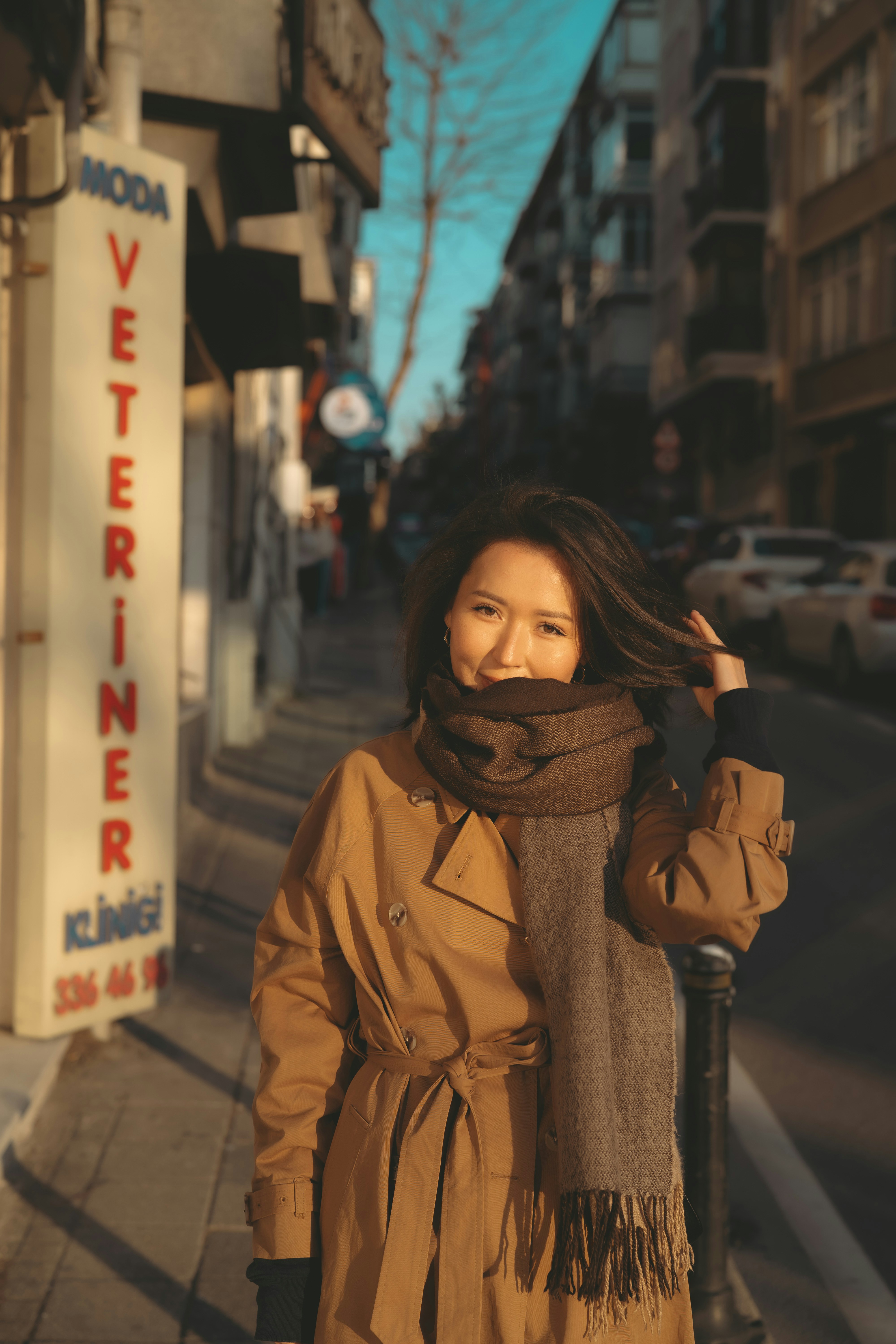 a woman in a trench coat is standing on a sidewalk