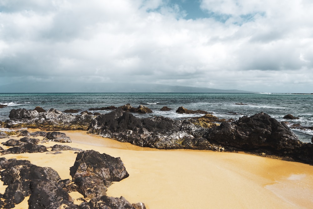 a sandy beach next to the ocean under a cloudy sky