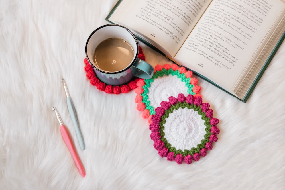 a cup of coffee and a crocheted coaster next to an open book