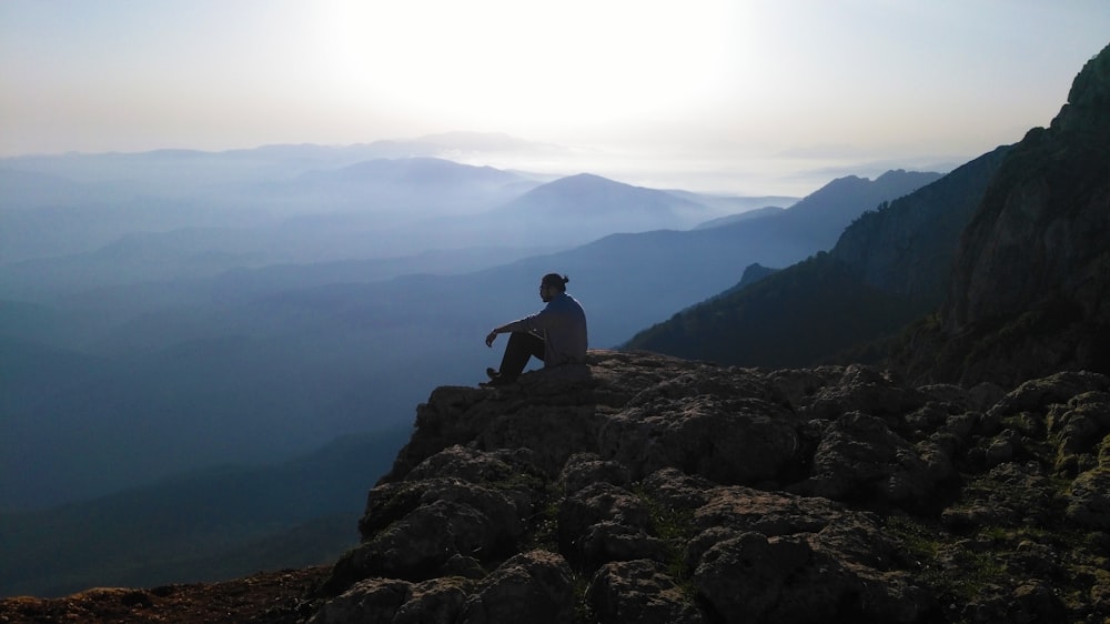 a man sitting on top of a mountain next to a cliff