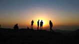 Sunset silhouette of a family enjoying a quiet moment together on a sandy hill.