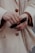 A close-up of hands holding a pair of sunglasses. One hand is adorned with gold rings, adding a touch of elegance to the scene. The coat buttoned in the background suggests a sophisticated fashion style.