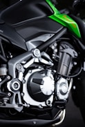 Close-up of a motorcycle engine showcasing mechanical parts with metallic finishes. The frame is sleek, emphasizing modern engineering with a touch of green detailing on the body.