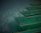 A series of elegant, translucent green steps with a glossy finish and golden edges, appearing to float against a misty, dark background. The design creates a sense of surrealism and futurism.