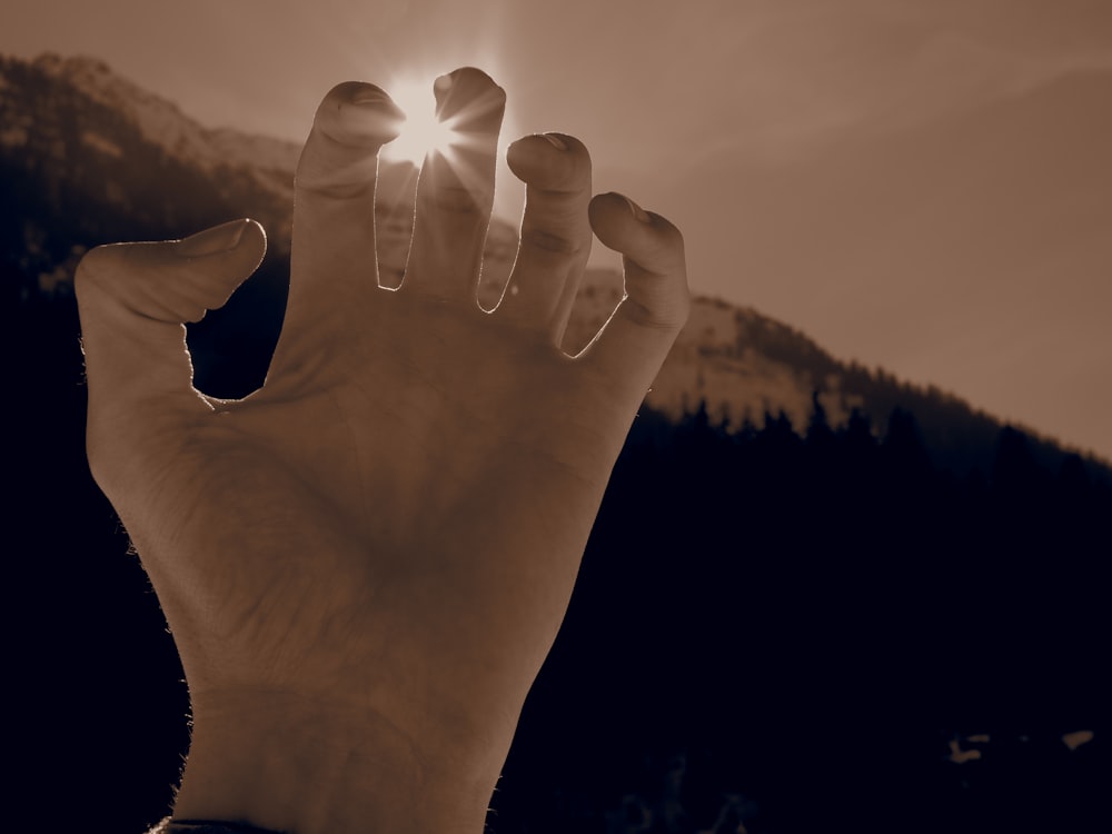 a hand reaching up towards the sun with mountains in the background