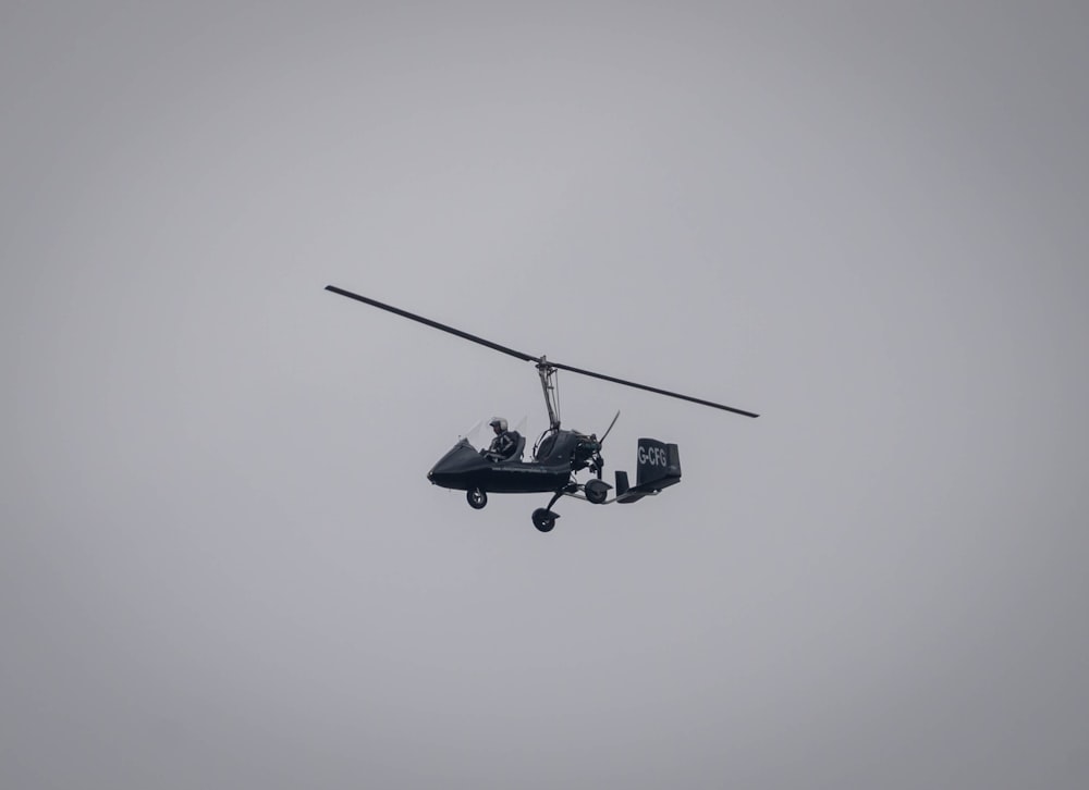 a helicopter flying through a gray sky with two people in it