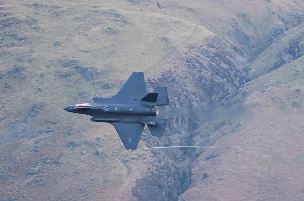 a fighter jet flying over a mountain range