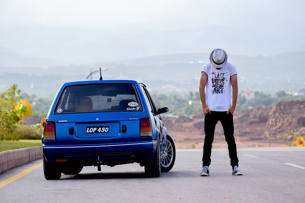 a man standing next to a blue car on a road