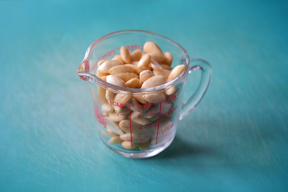 a measuring cup filled with peanuts on a blue surface
