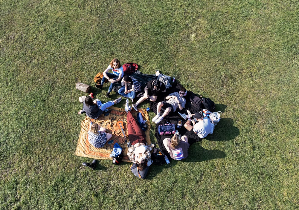 a group of people sitting on top of a grass covered field