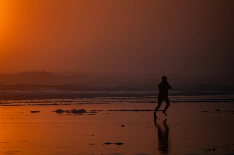 Sunset silhouette of a person running along the beach wearing aurora sportswear.