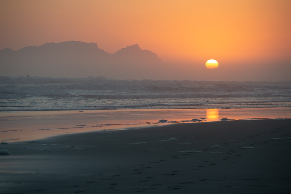 the sun is setting over a beach with footprints in the sand