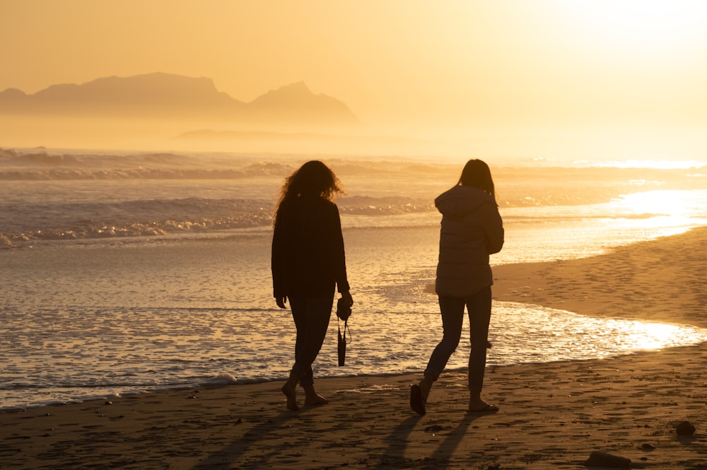 two women walking on the beach at sunset