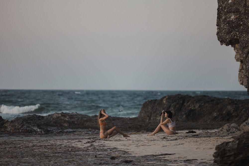 two women sitting on the beach taking pictures