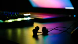 Stylish earbuds with luminous blue accents resting on a dark, minimalistic surface with subtle neon glow.