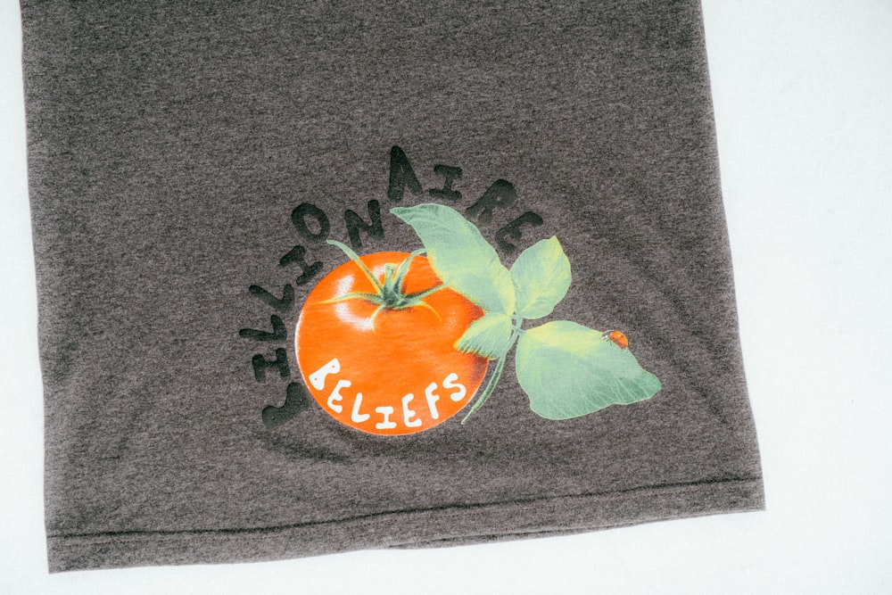 una camicia grigia con un'arancia e foglie su di essa