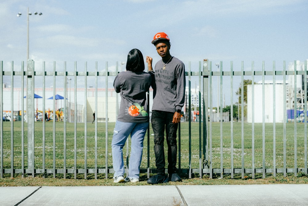 a couple of people standing next to a metal fence