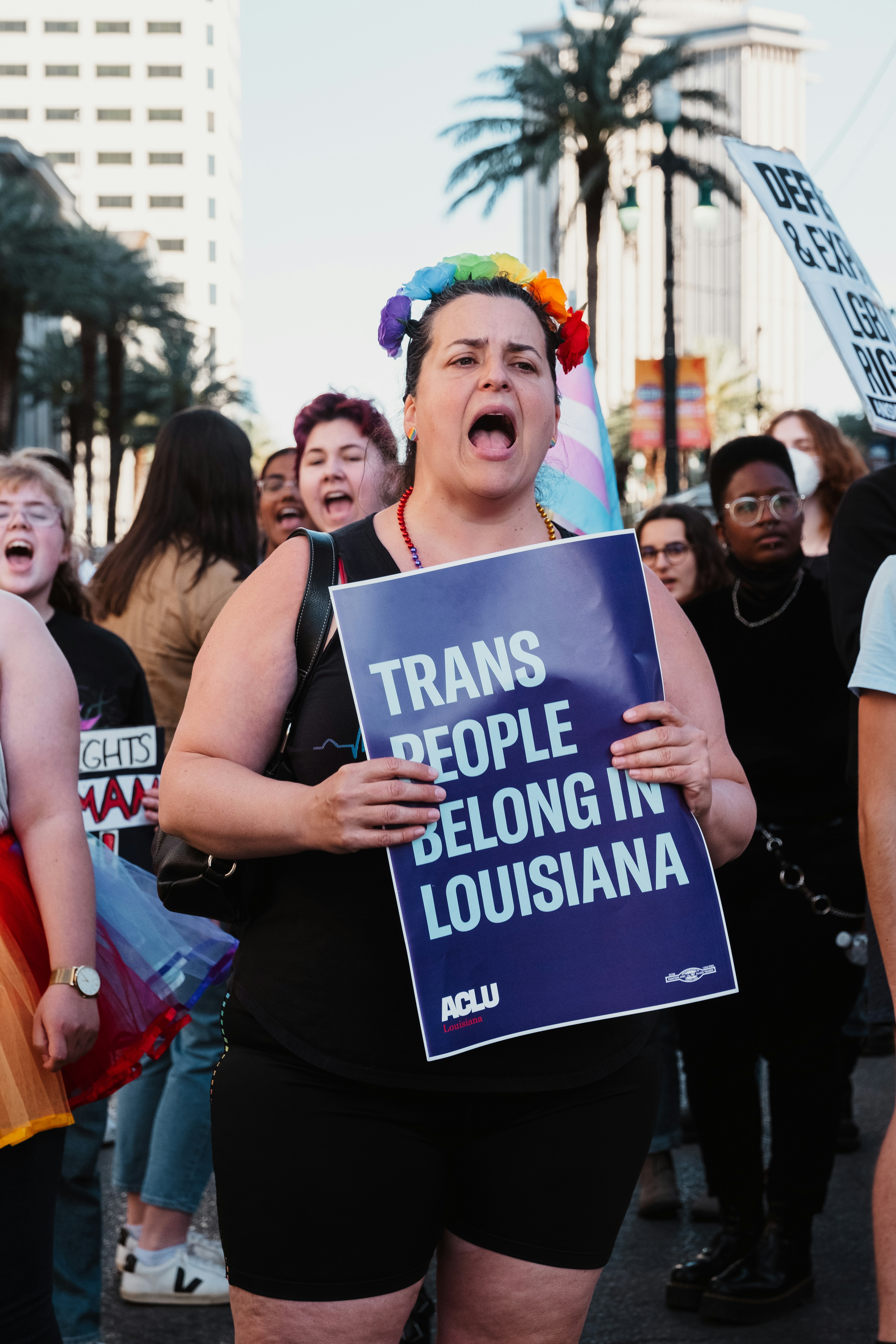a woman holding a sign that says transs people belong in louisiana