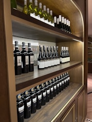A wooden wine rack displaying multiple rows of neatly arranged wine bottles. The shelves contain bottles of red and white wine, each aligned in an orderly manner. The labels on the bottles are visible, highlighting the variety of wines available.