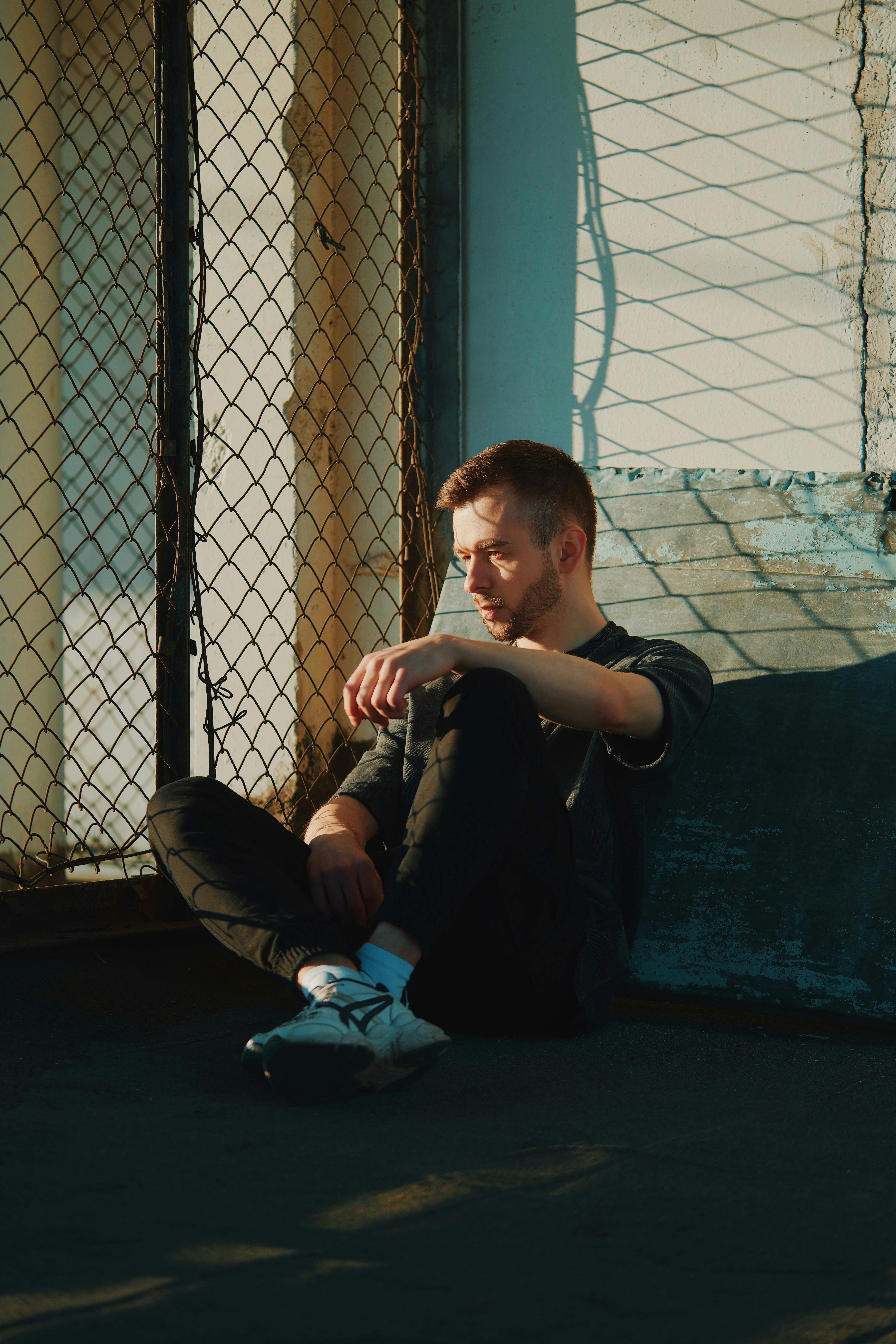 a man sitting on the ground next to a fence