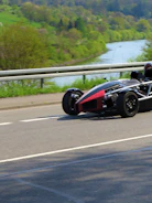 Mazda MX-5 roadster with top down on a coastal road under clear skies.