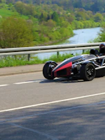 A Ferrari F8 cruising through a scenic alpine valley with vibrant greenery.