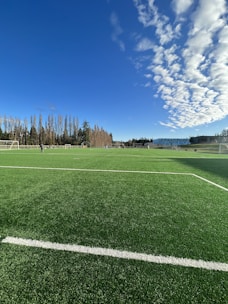 A group of young soccer players practicing on a grassy field under a clear blue sky.
