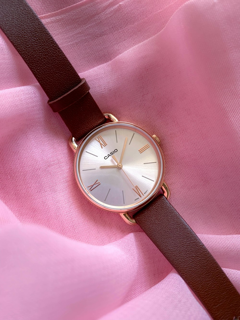 a close up of a watch on a pink cloth