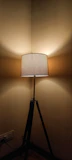 A tripod standing lamp with a warm fabric shade standing next to a cozy reading chair.