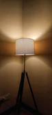 A tripod floor lamp standing tall beside a comfy armchair in a modern living room.