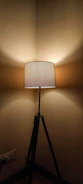 A tripod standing lamp with a warm fabric shade standing next to a cozy reading chair.