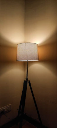 A tripod floor lamp standing tall beside a comfy armchair in a modern living room.