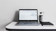 A minimalist desk featuring a notebook, pen, and a cup of coffee beside a tablet showing analytics.