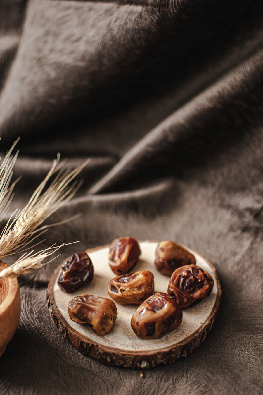 Whole dates on a wood slice beside wheat ears on a dark cloth