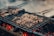 Juicy pieces of meat are sizzling on a grill, positioned over glowing charcoal embers. The scene captures the essence of a barbecue with a smoky and rustic appeal, enhanced by the visible grill marks on the meat.