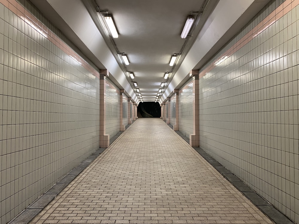 a long hallway with white tiles and a black tunnel