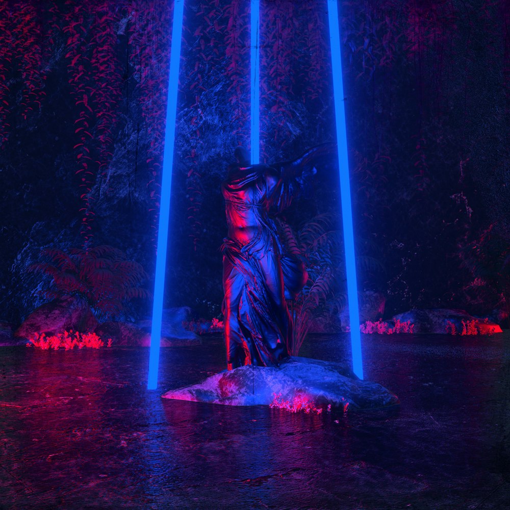 a statue in the middle of a pond surrounded by blue and red lights